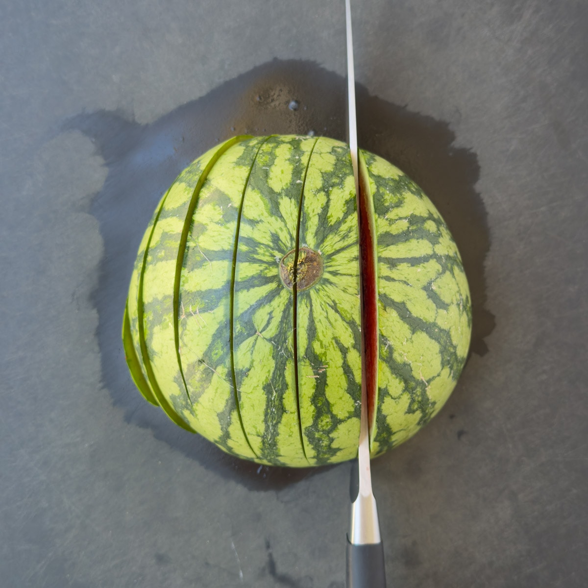 Cutting a watermelon half crosswise into 1-inch slices.