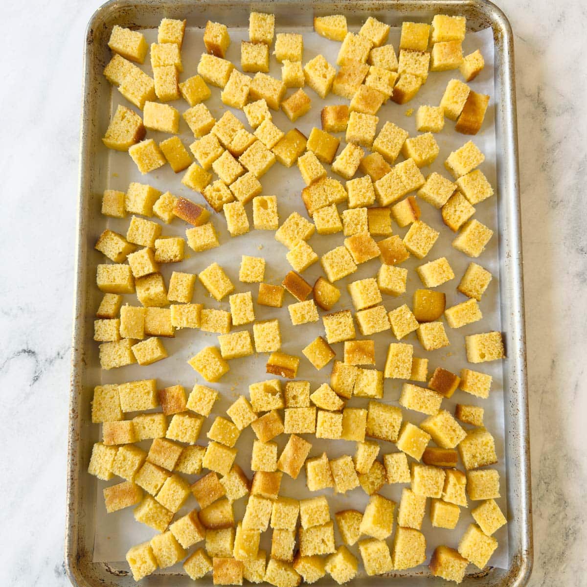 Homemade cornbread cubes on a baking sheet with parchment