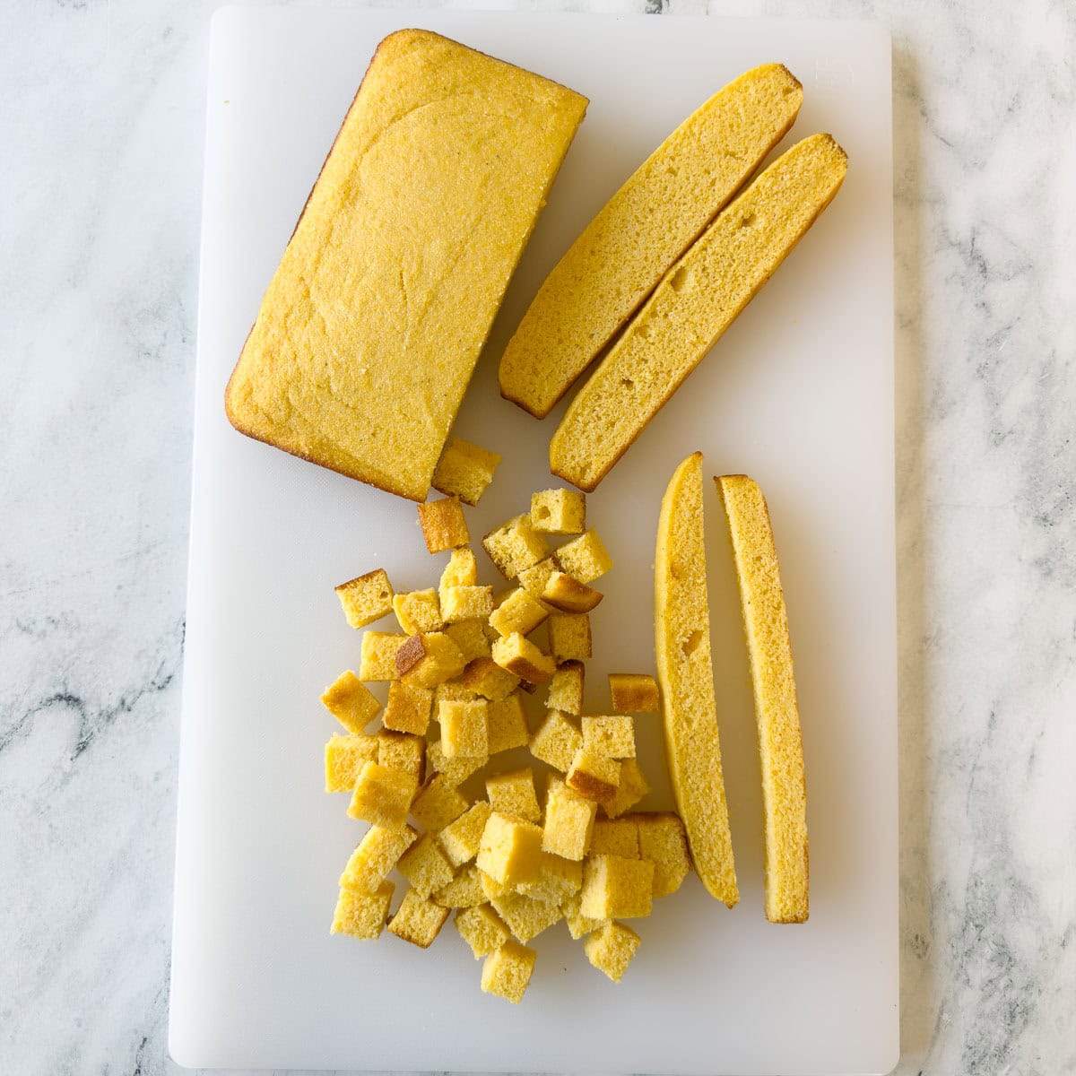 Slicing a loaf of cornbread into cubes for gluten free cornbread dressing to be dried.
