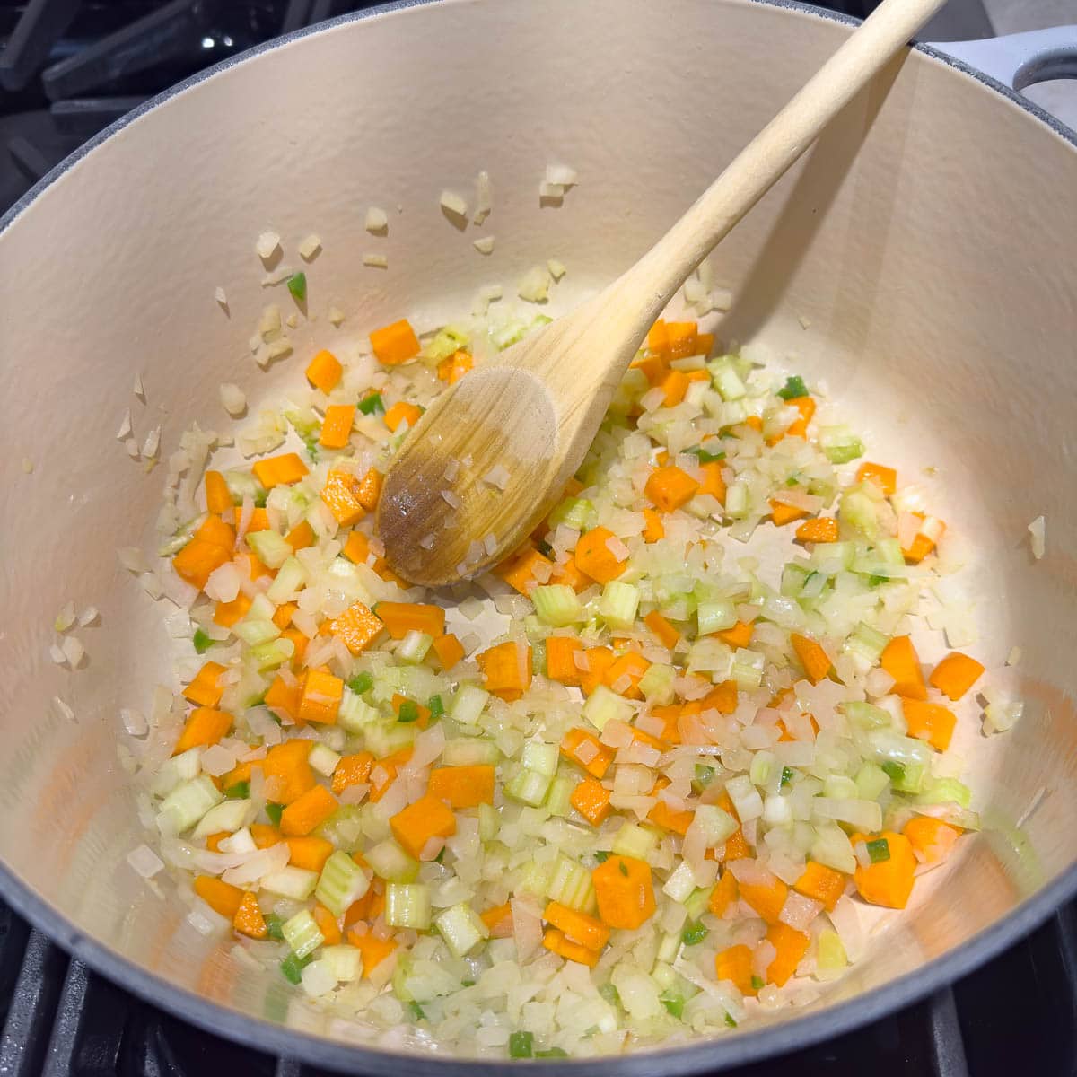 Sauteing onion, carrot, and celery for soup in a pot on stovetop.
