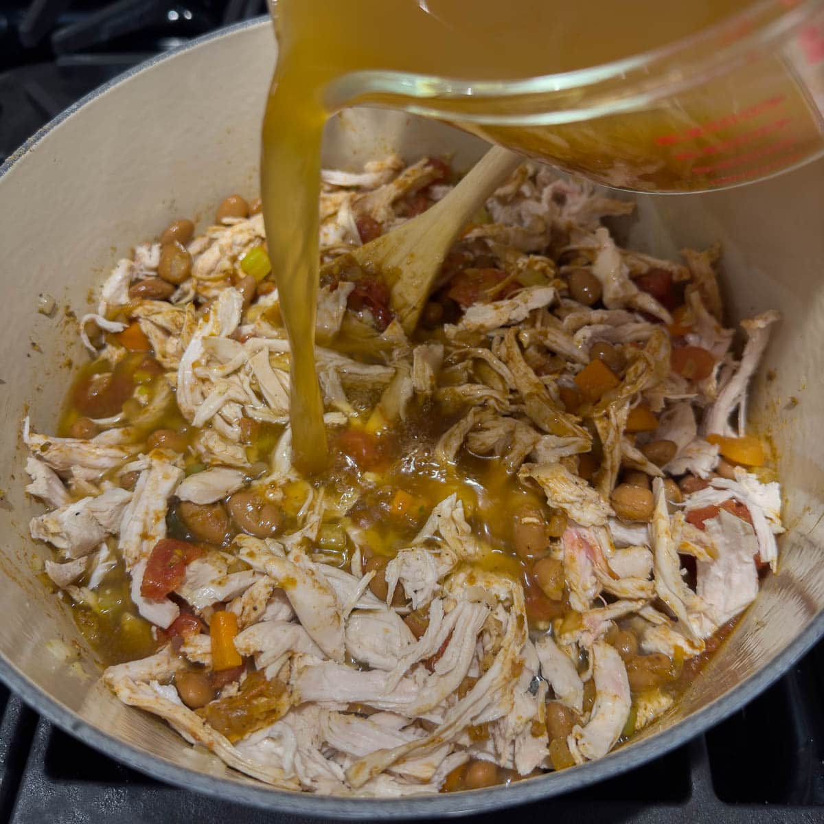 Adding shredded chicken and broth to the pot to complete the soup.