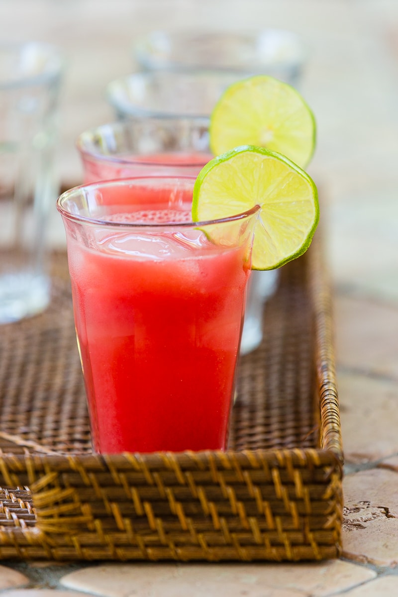 A glass of beautiful red watermelon agua fresca with a lime slice for garnish on a basket tray.
