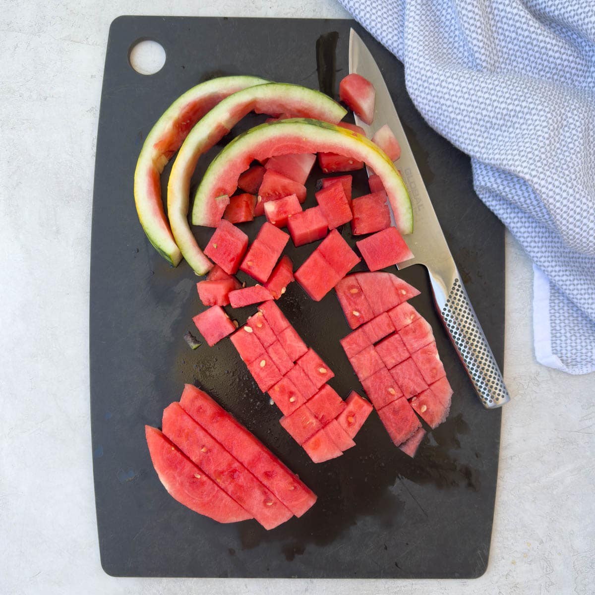 Cutting up a red watermelon into chunks on a black cutting board.