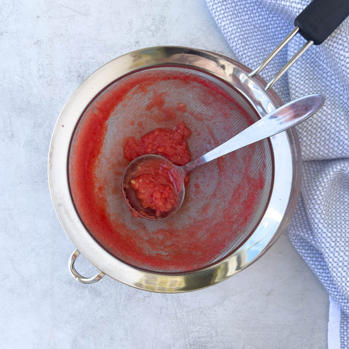 Watermelon pulp in a stainless steel strainer with a ladle.