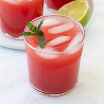 A glass of bright red watermelon agua fresca with mint and ice.
