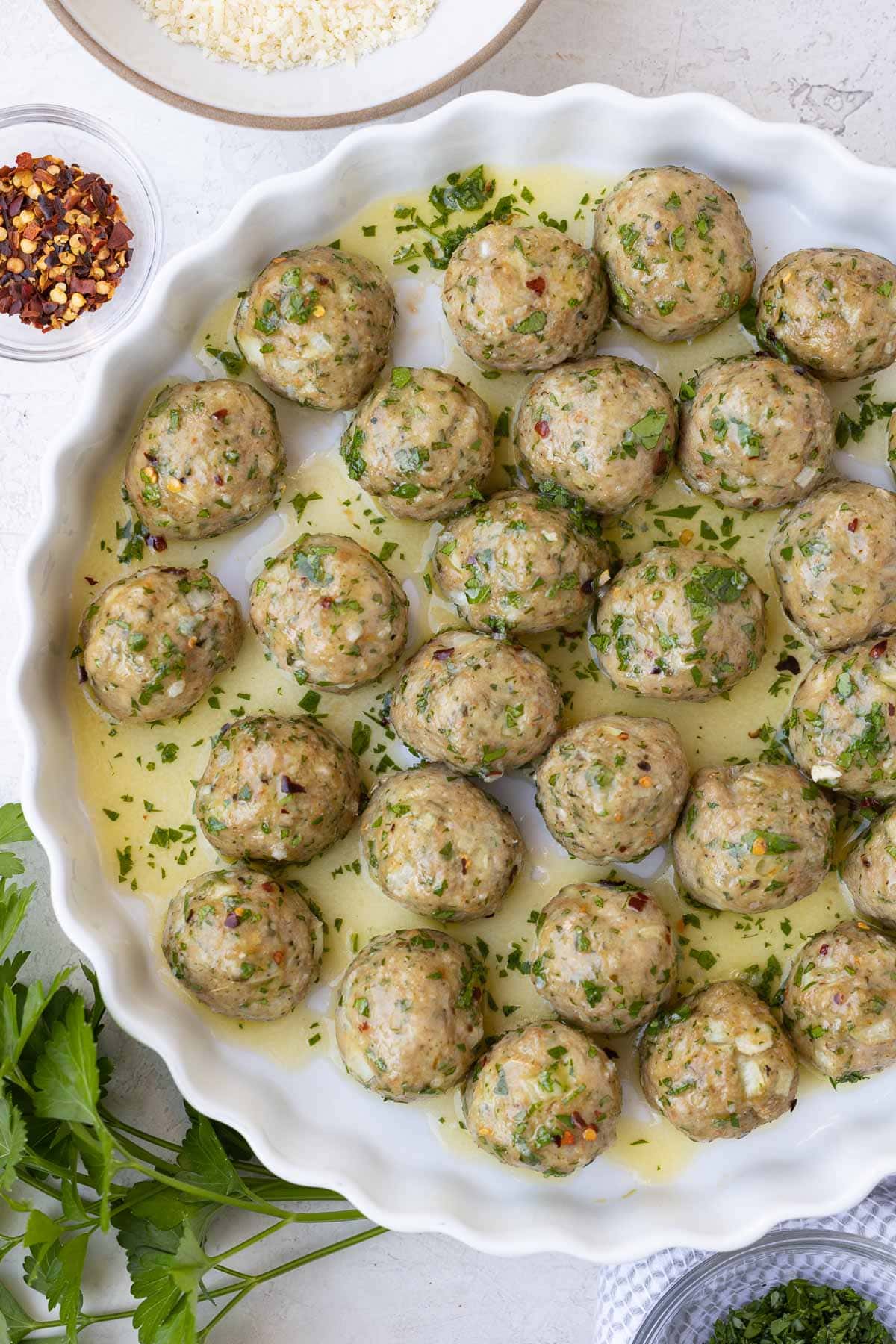 Turkey meatballs in a butter, olive oil, garlic sauce in a white dish with parsley. 