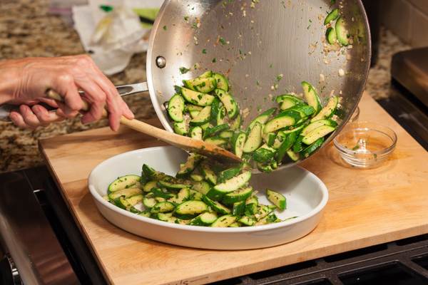Pouring cooked zucchini into a shallow casserole dish for baking.