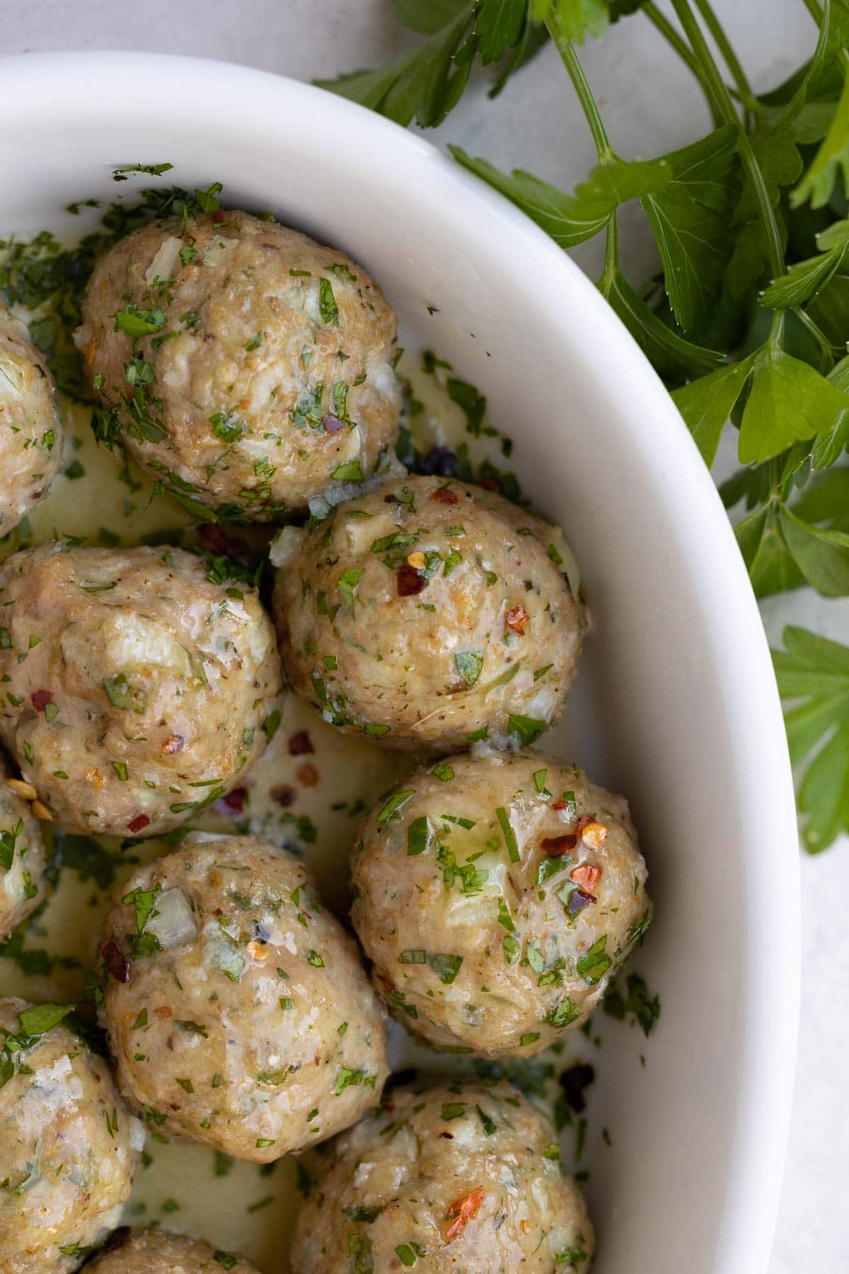 A close up of meatballs in a shallow white casserole dish with a buttery garlic sauce. 