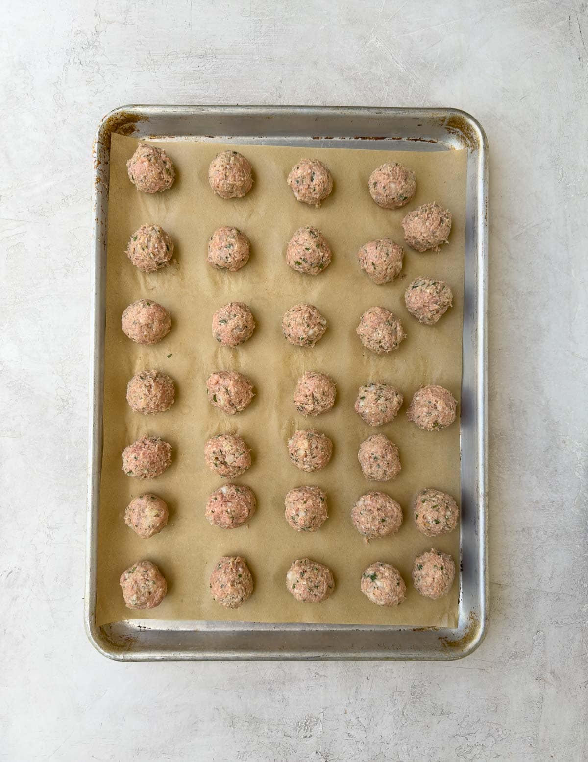 Rolled meatballs on a rimmed baking sheet with parchment for oven baking.
