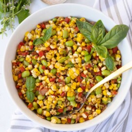 A colorful bowl of sweet corn succotash with yellow corn, red and green peppers, and edamame.