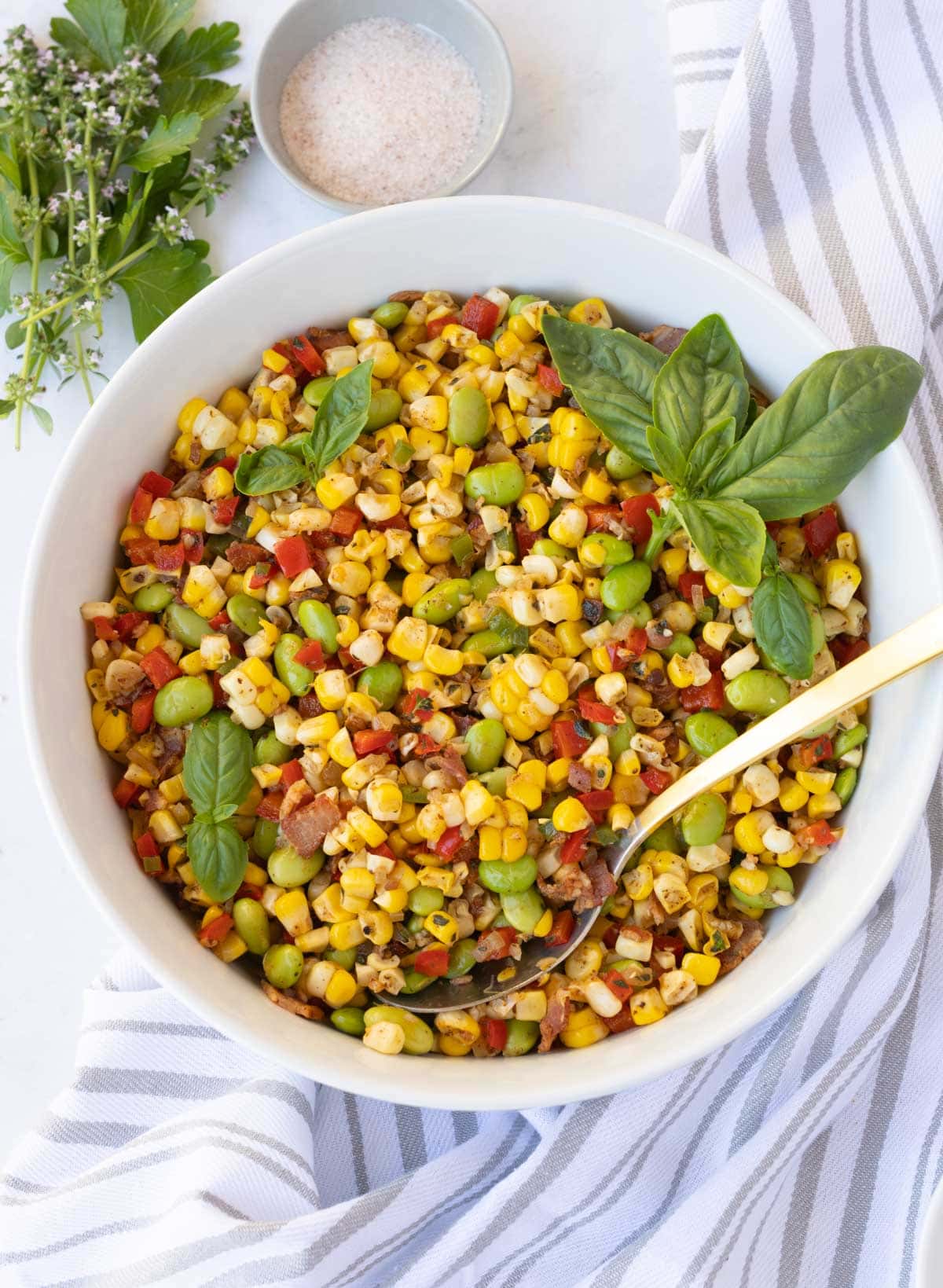 A colorful bowl of sweet corn succotash with bacon, yellow, red and green in a white bowl.