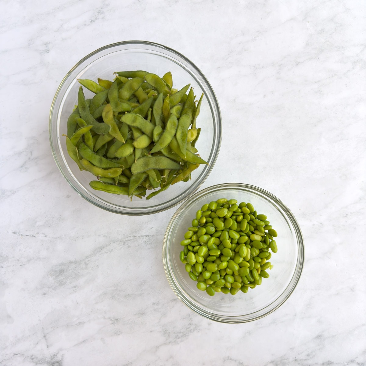 Shelled edamame and spent pods in glass bowls.