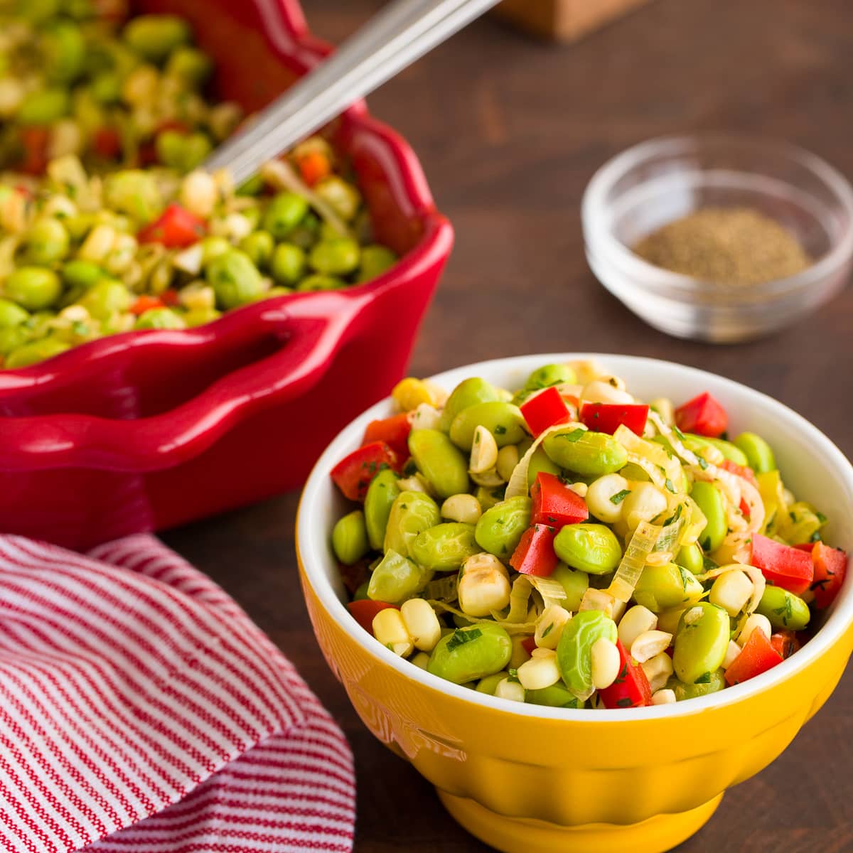 Colorful edamame succotash in yellow bowls on a wood table.