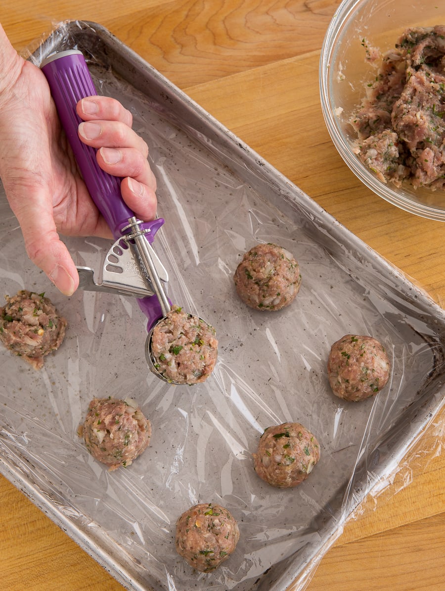 Portioning turkey meatball mix into balls with a cookie scoop onto a baking sheet.