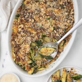 Zucchini casserole topped with browned curst of breadcrumbs and parmesan, with silver spoon.