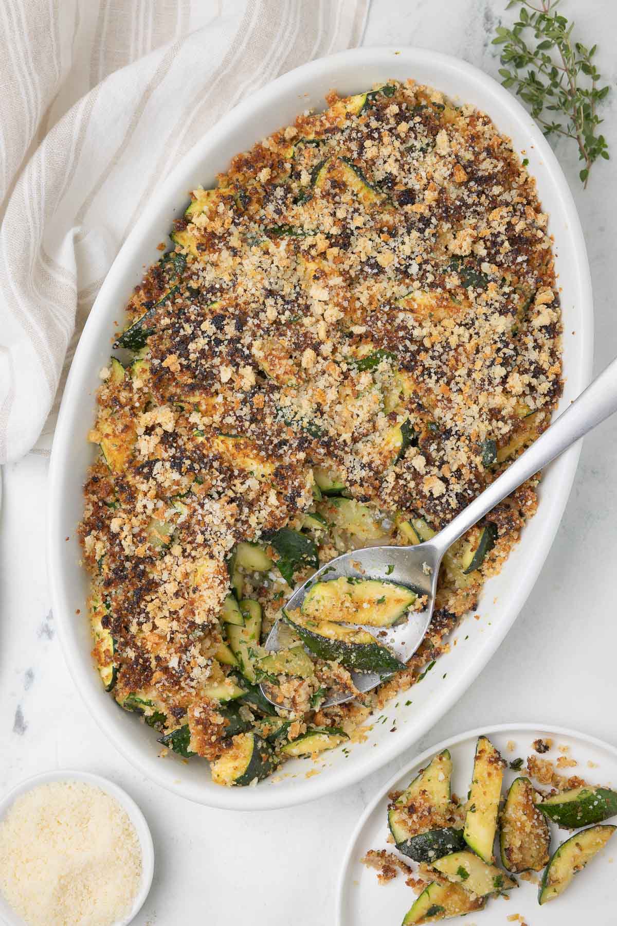 Zucchini casserole with crusty top of breadcrumbs and parmesan cheese and large serving spoon.