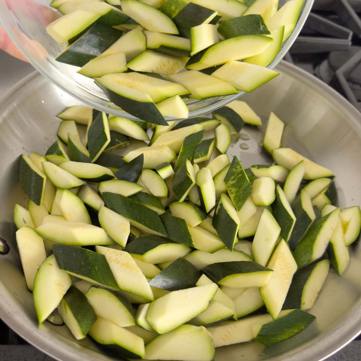 Sliced zucchini pouring into a pan with olive oil for sautéing.