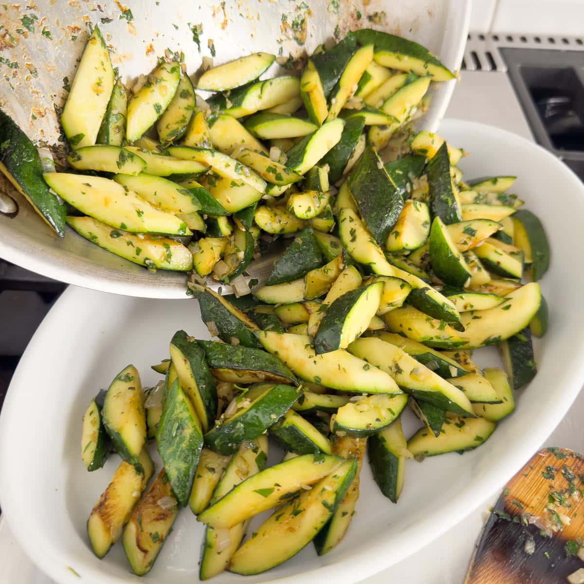 Zucchini pouring into an oval baking dish for a zucchini casserole.