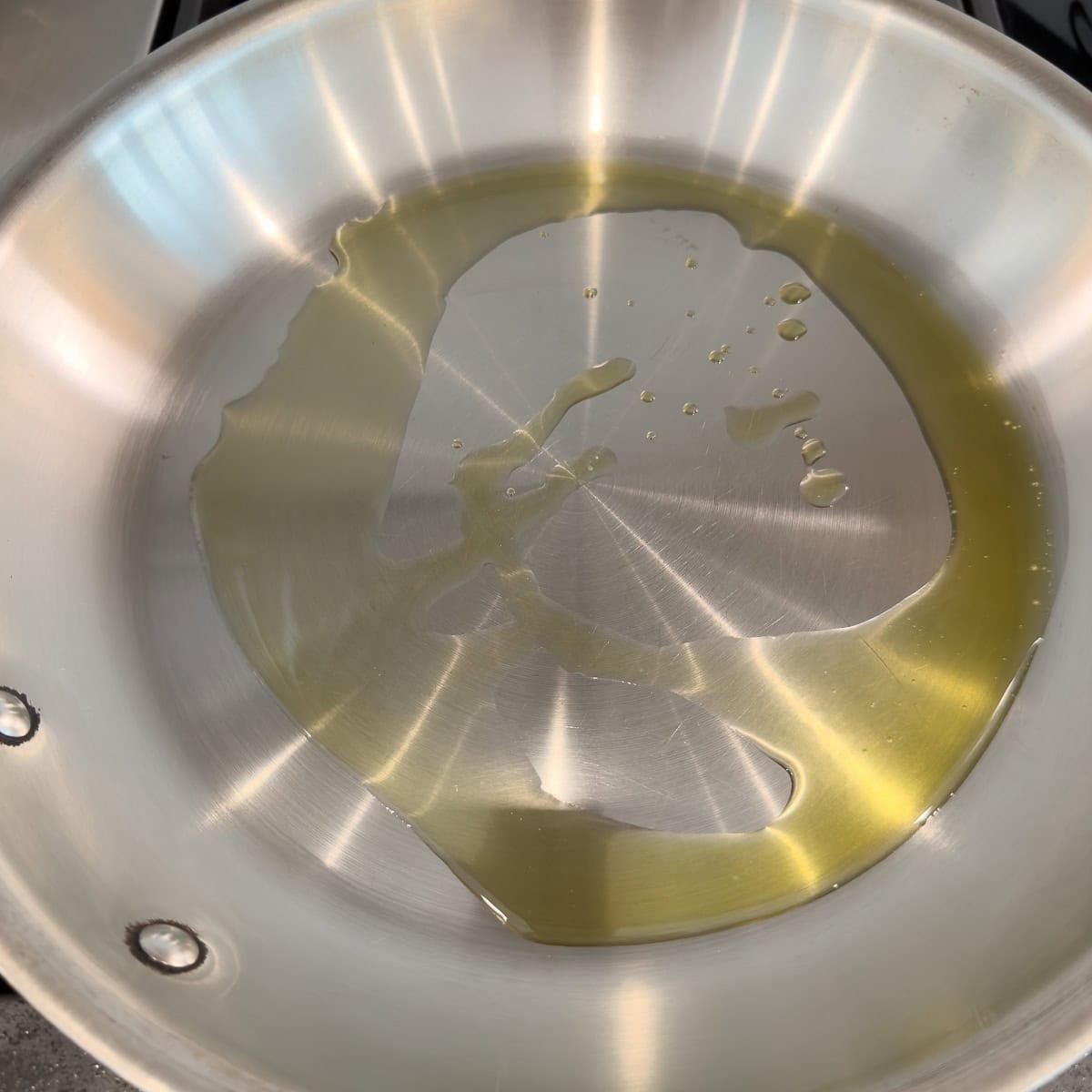 Olive oil heating in a stainless steel pan on teh stovetop.