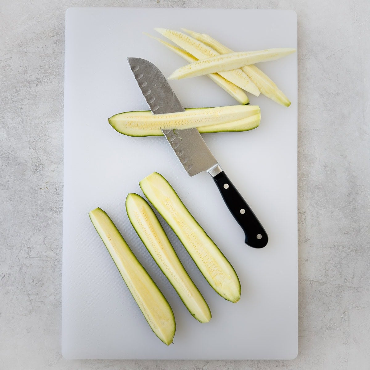 Trimming zucchini of seedy centers on a white cutting board.