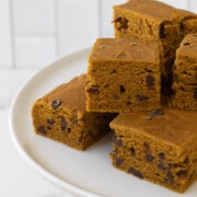 Squares of pumpkin brownies with chocolate chips on a white cake stand.