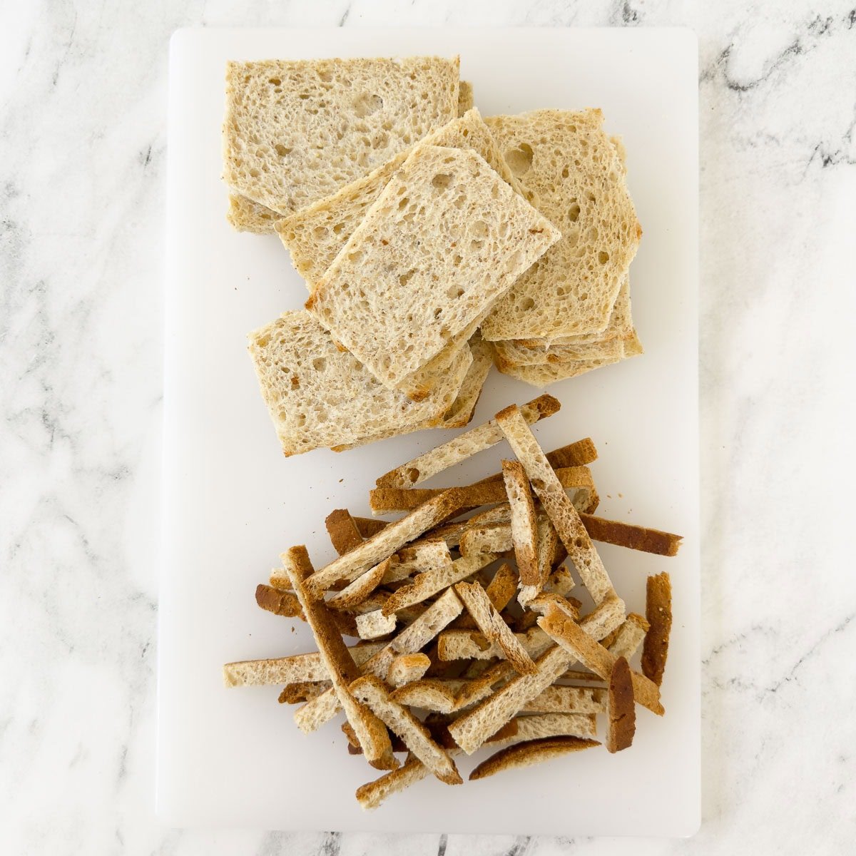 A cutting board with bread slices trimmed of crusts.