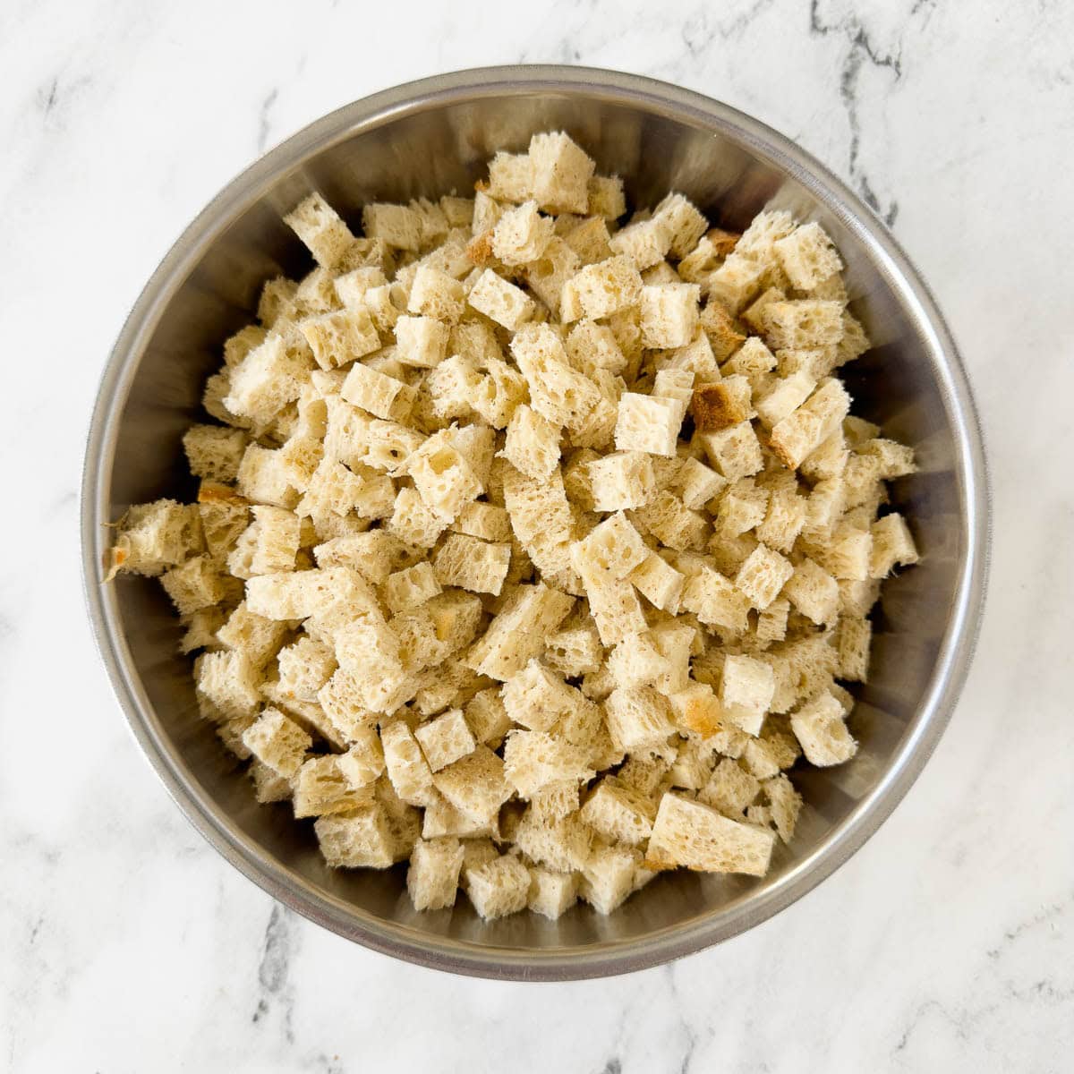 A steel bowl of cubed bread for making breadcrumbs.