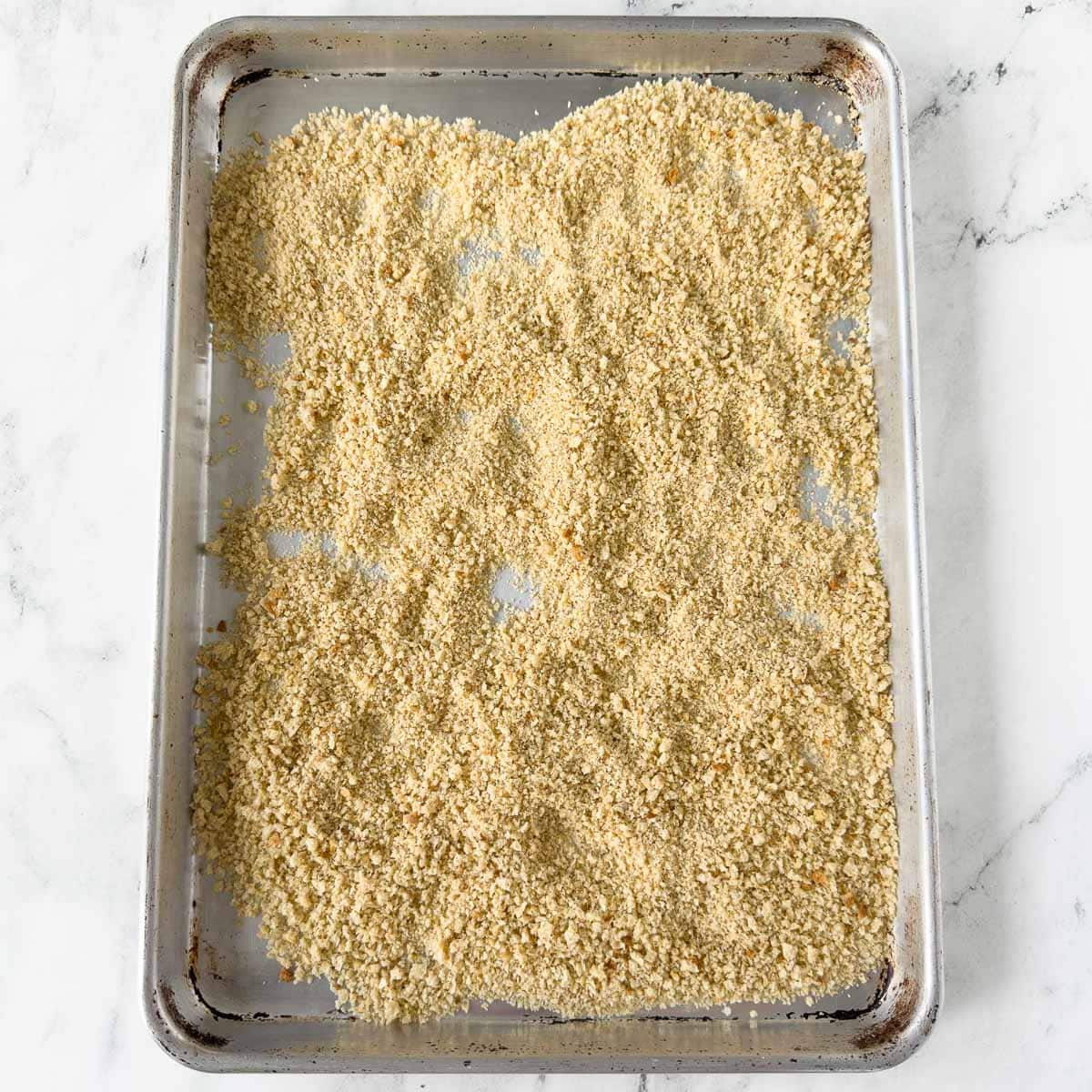 Breadcrumbs finished baking into toasted crumbs on a rimmed baking sheet.