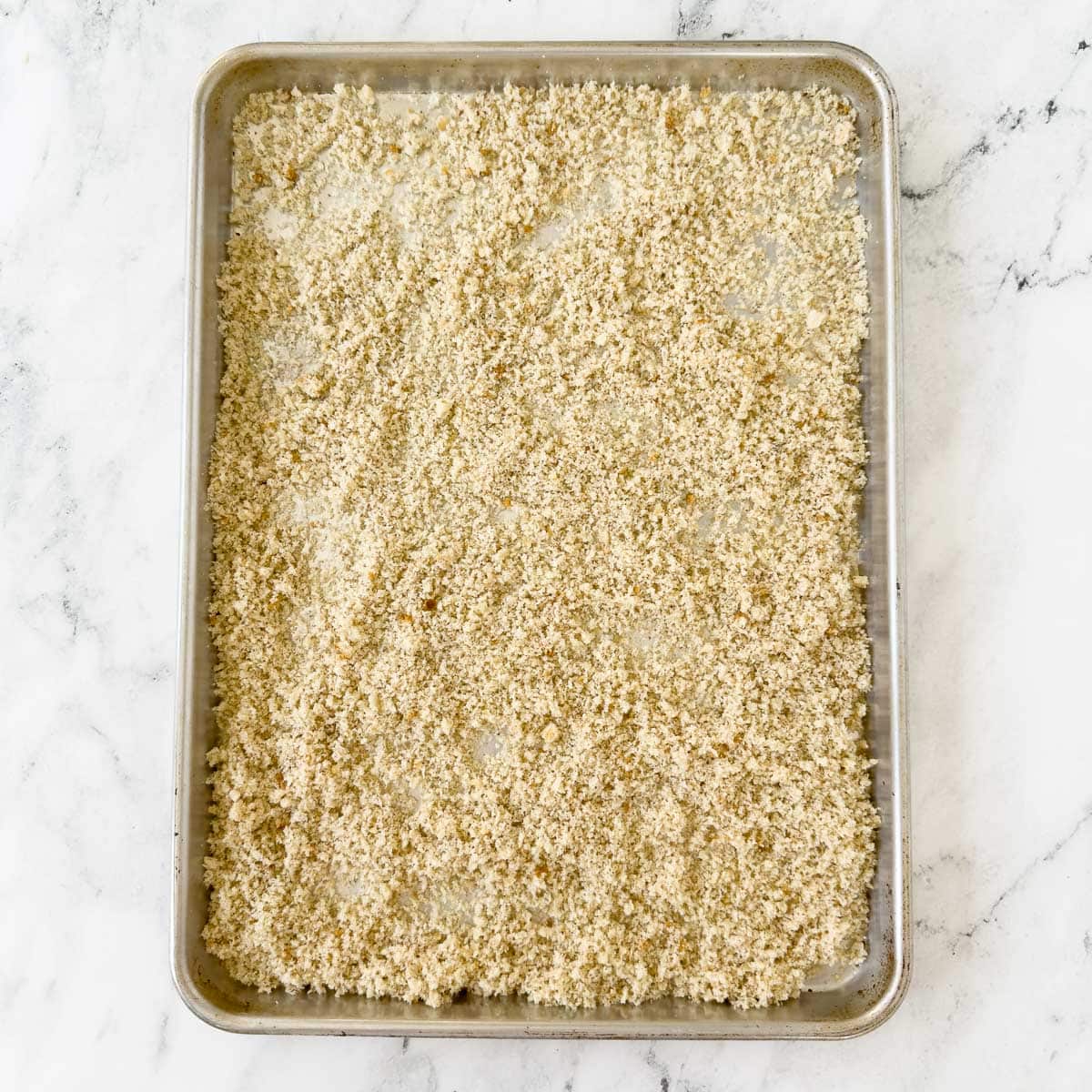 Bread crumbs scatter on a rimmed baking sheet for baking.