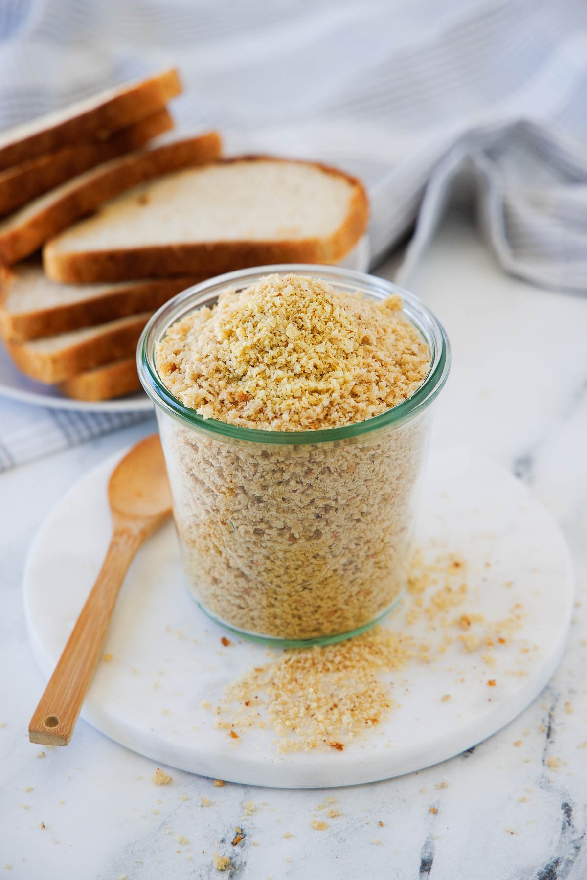A tall jar of homemade golden breadcrumbs on a round white plate.