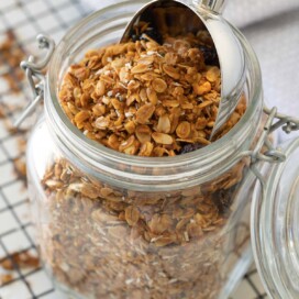 A glass jar of freshly baked granola with a scooper in the top.