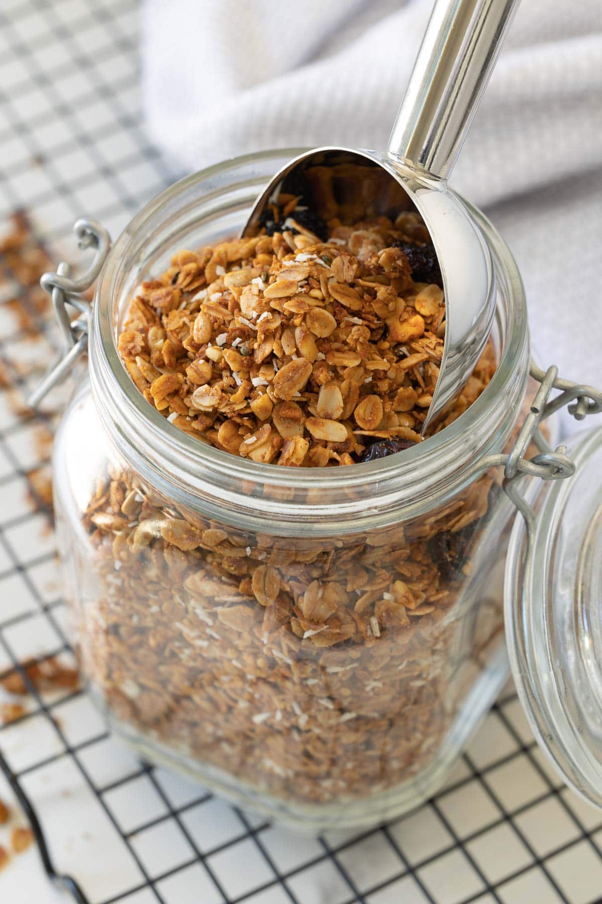 A glass jar of freshly baked granola with a scooper in the top.