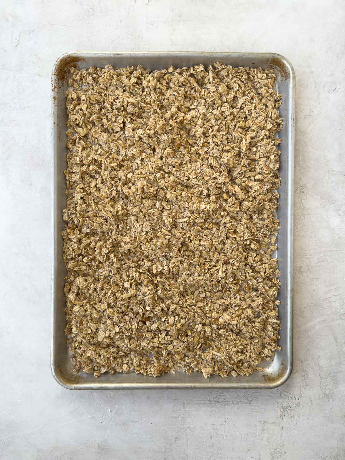 Spreading granola mixture onto a baking sheet for baking.