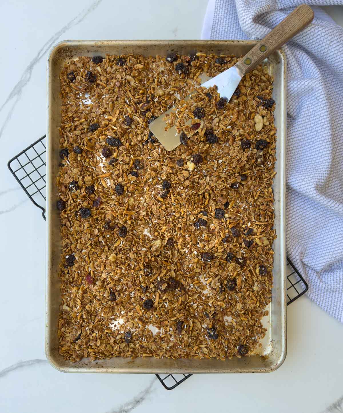 Baked granola cooling on a rack with a metal spatula to stir.