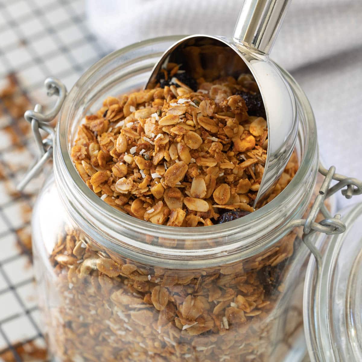 A close up of an open jar of homemade granola with a silver scoop.