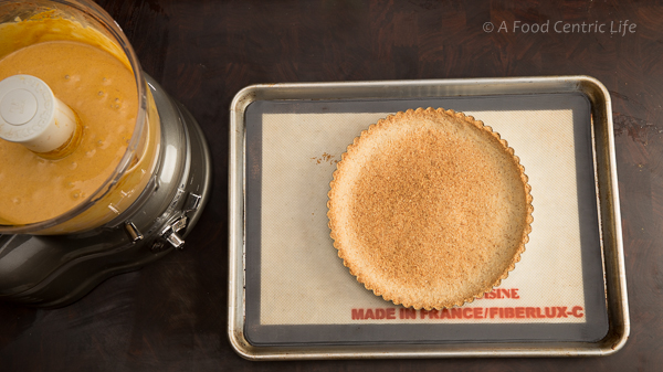 A baked tart crust and pumpkin filling ready to pour in food processor. 