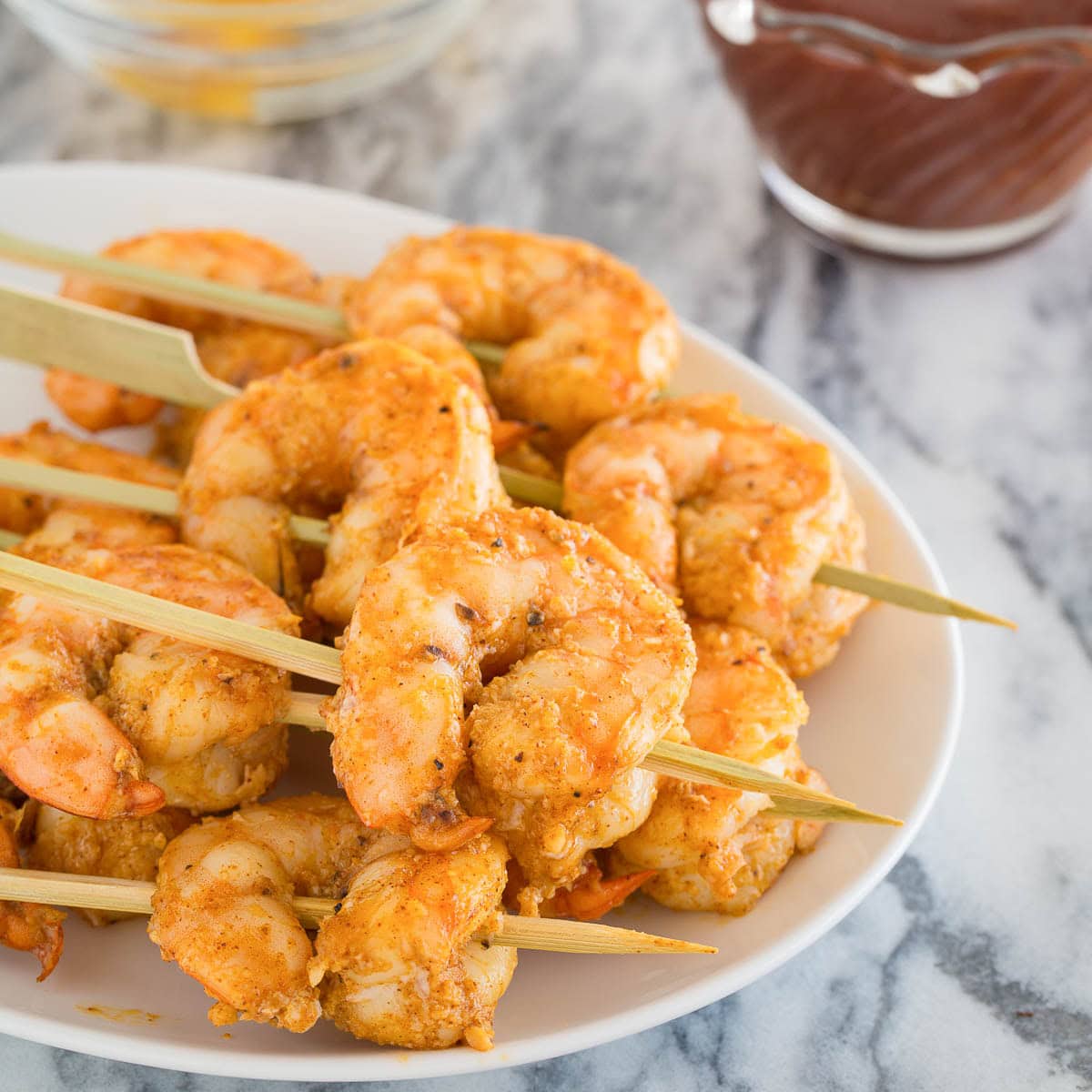 A small appetizer plate of golden baked shrimp on wooden skewers with cocktail sauce.