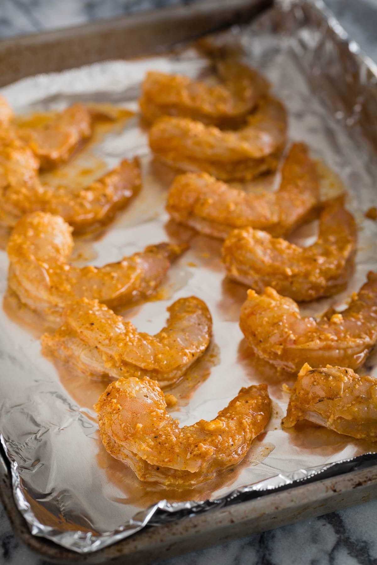 Raw marinated shrimp arranged on a foil covered baking tray.
