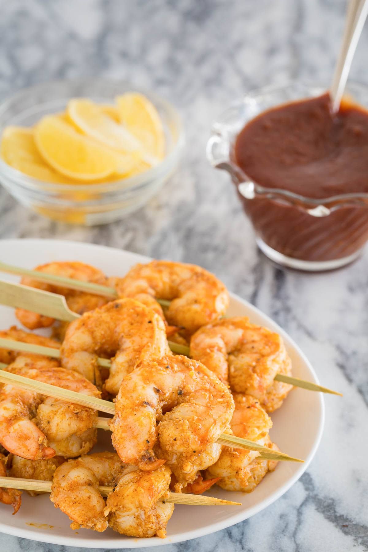 A small plate of garlic baked shrimp on skewers with lemon wedges and cocktail sauce.