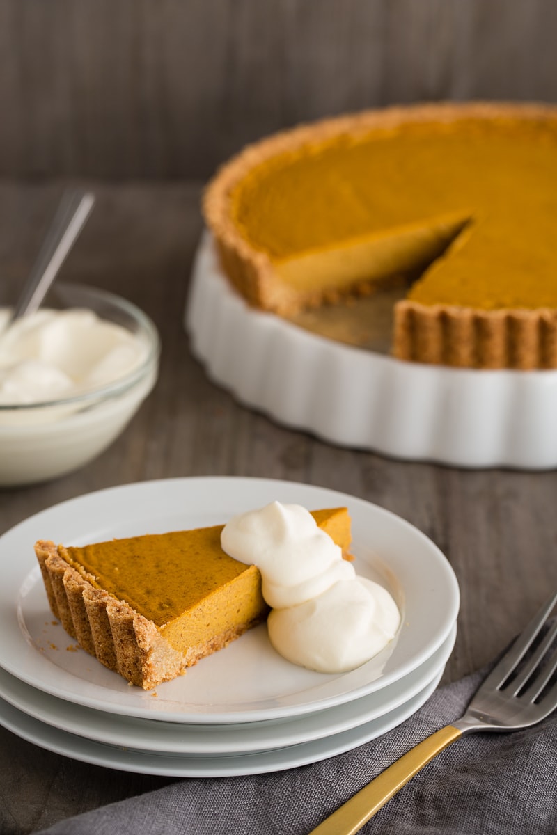 A piece of pumpkin tart on a white plate with soft whipped cream.