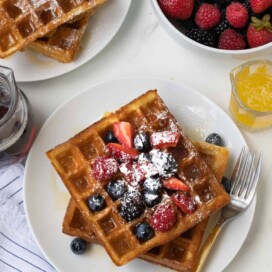 Plates of golden Belgian waffles with fresh berries and maple syrup.