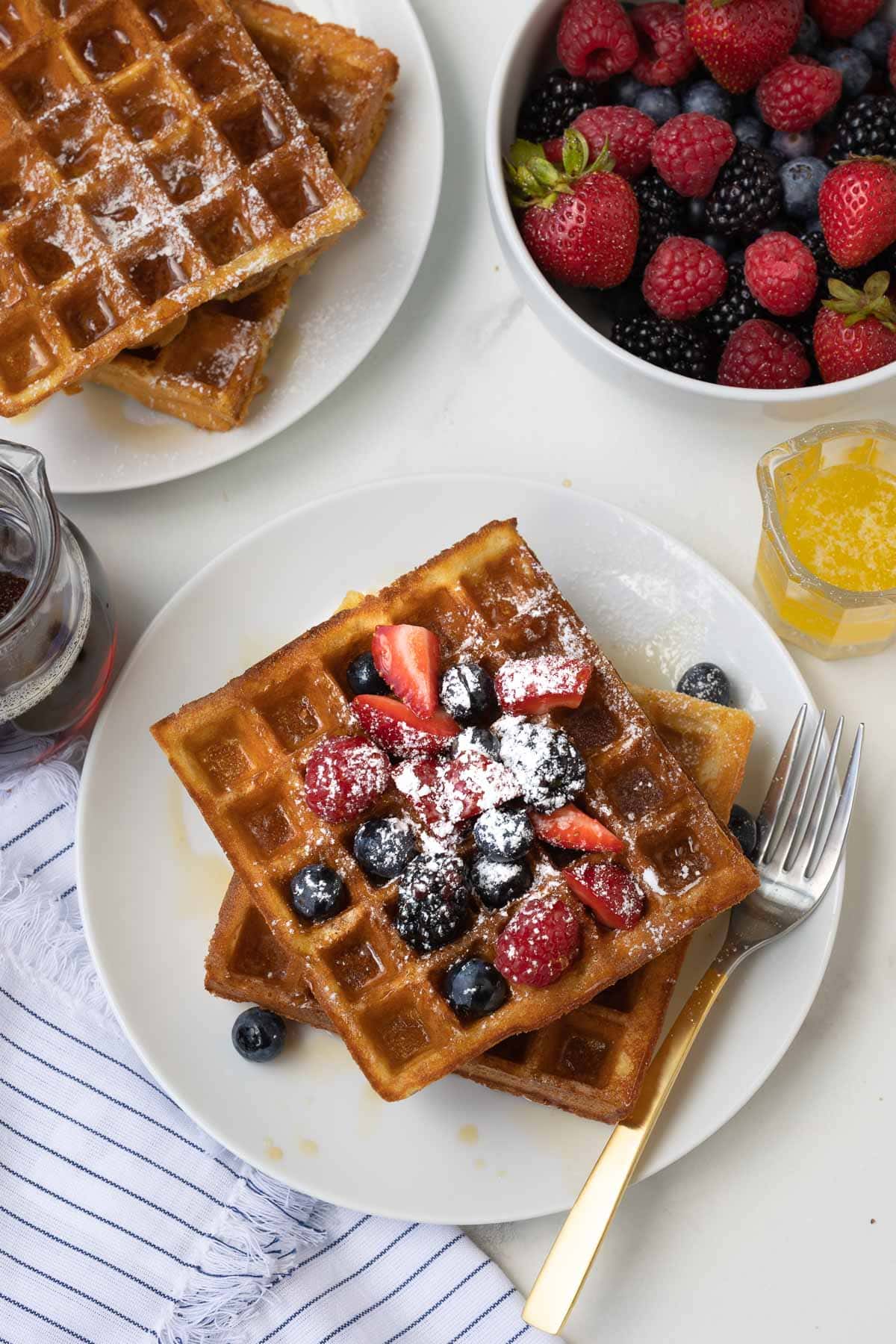 Plates of golden Belgian waffles with fresh berries and maple syrup.
