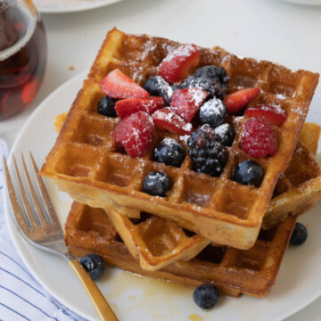 Close up of crispy golden waffles with blueberries, raspberries, strawberries.