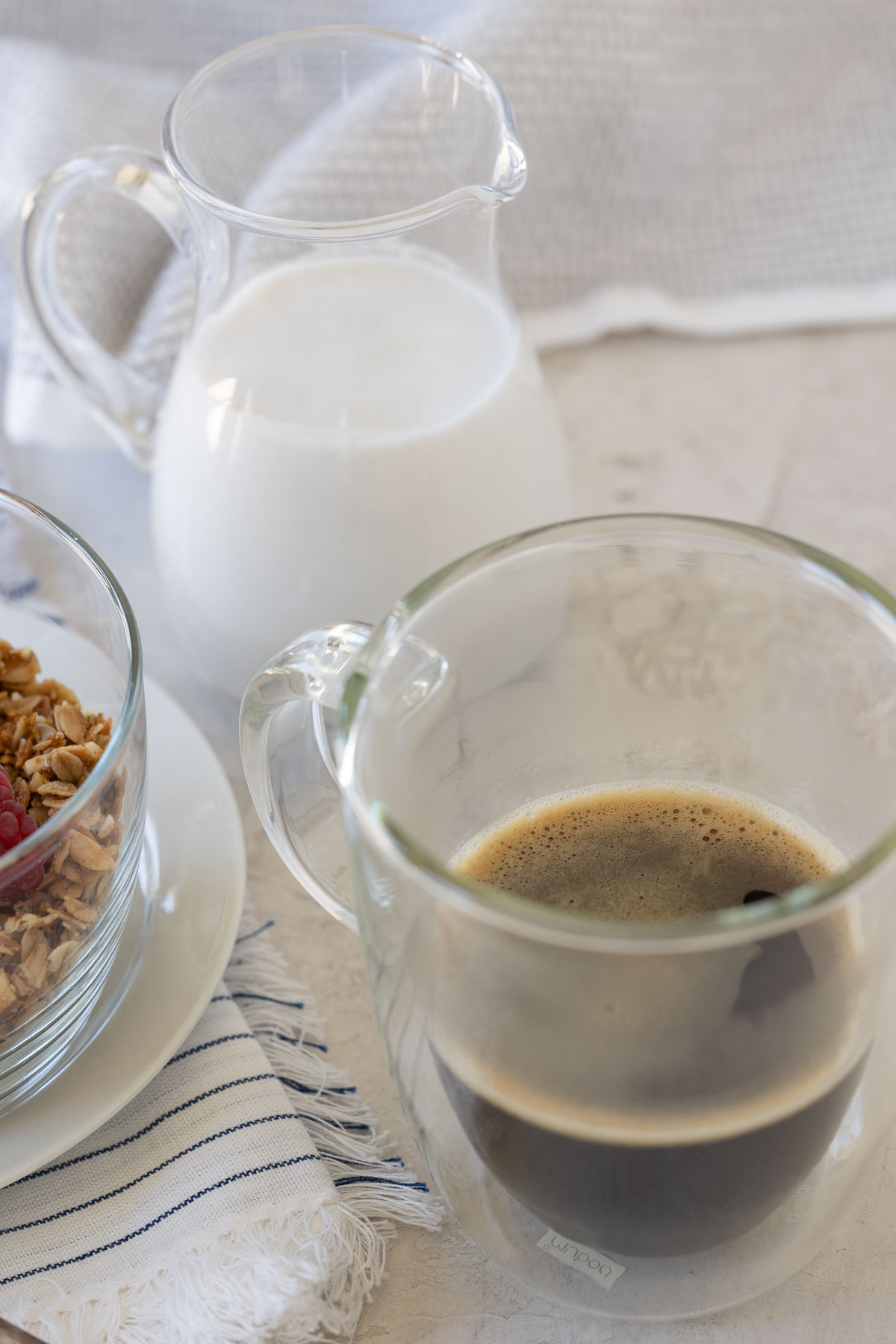 Breakfast setting with granola, berries, coffee and pitcher of milk.