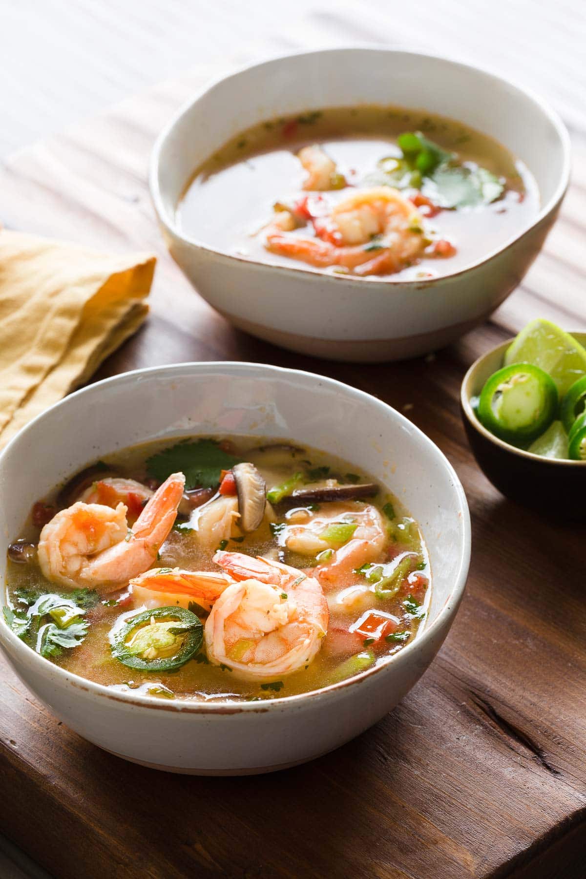 Brothy shrimp Tom Yum soup in rustic bowls with chile peppers, vegetables, and limes.