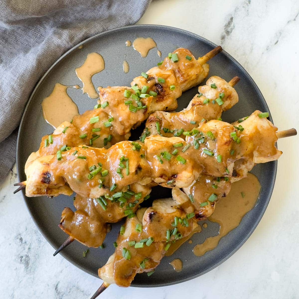Creamy almond butter Asian dipping sauce drizzled over grilled chicken skewers on a gray plate.