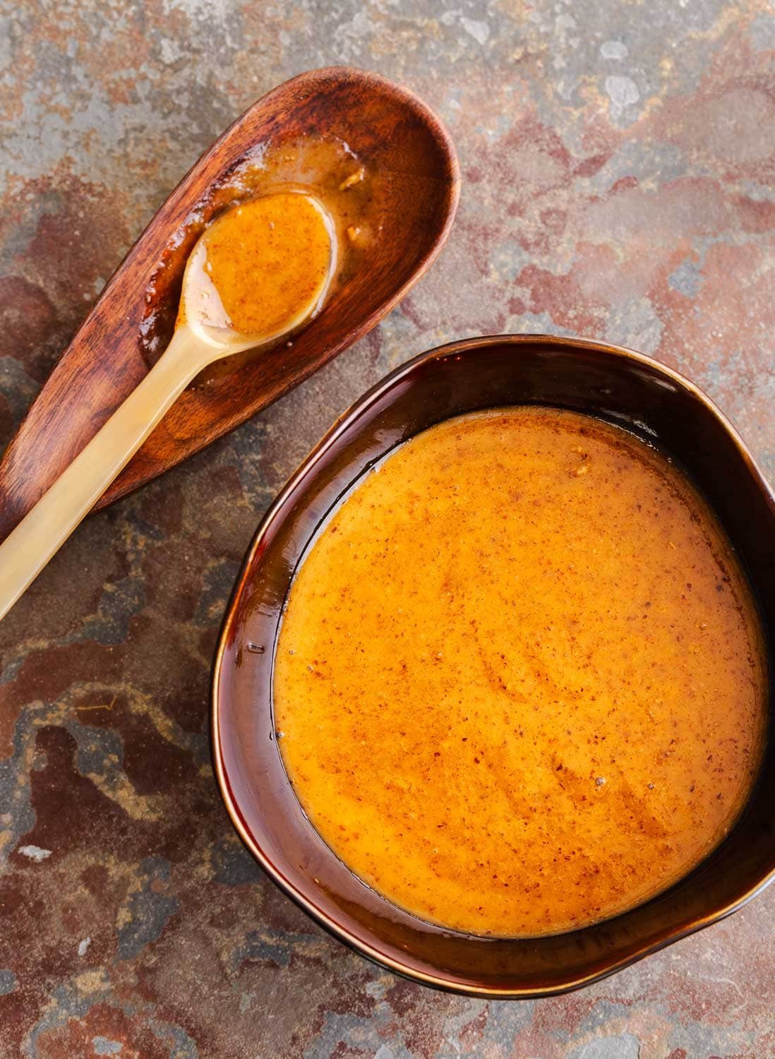A brown bowl of creamy golden brown Asian dipping sauce and a spoon on the side.