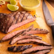 Sliced flank steak on a cutting board with flank steak marinade in a small bowl.