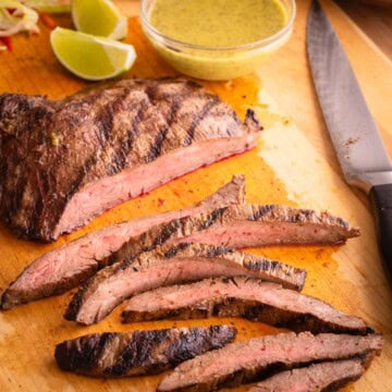 Sliced flank steak on a cutting board with flank steak marinade in a small bowl.