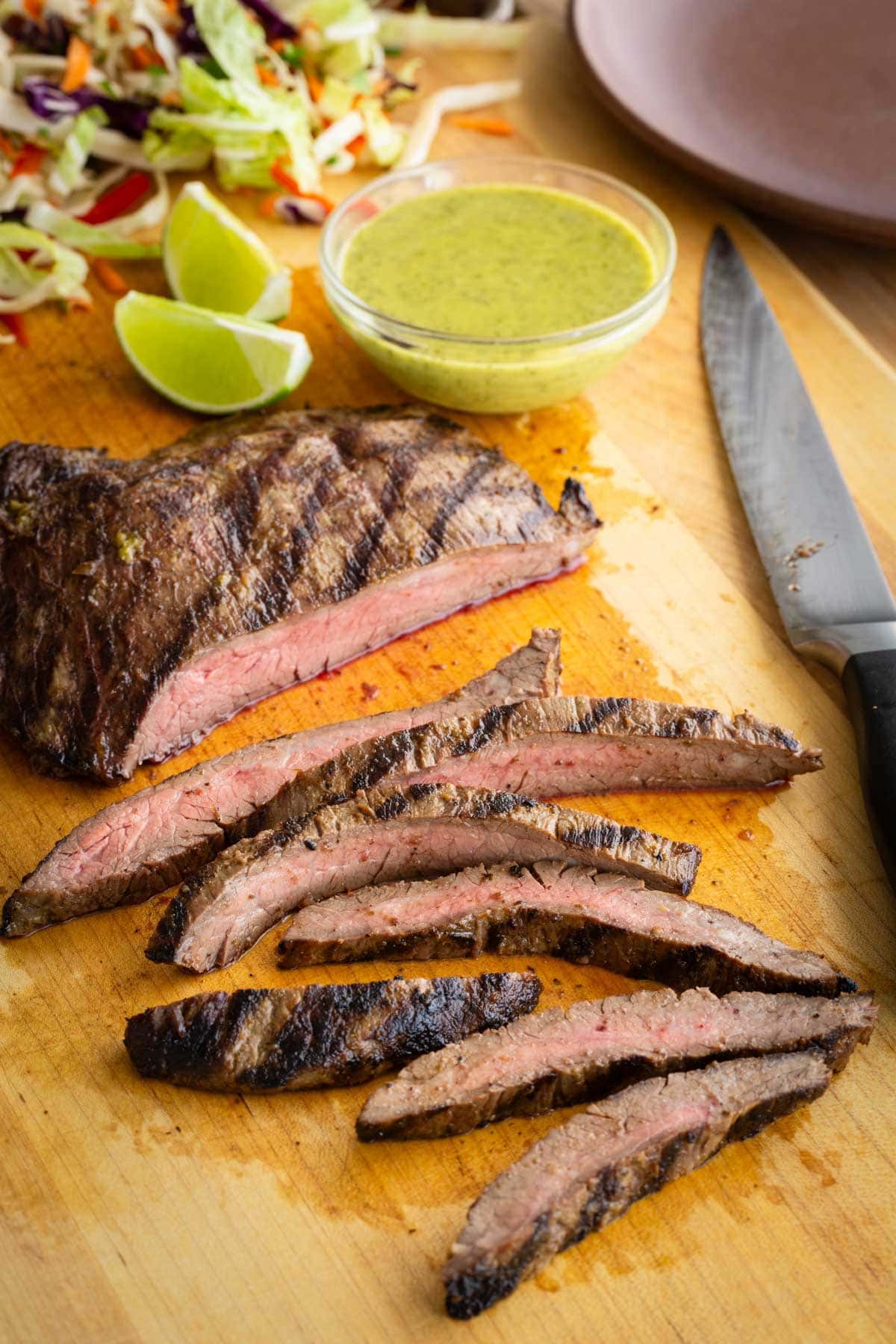 Grilled carne asada steak on a wood cutting board with a knife.
